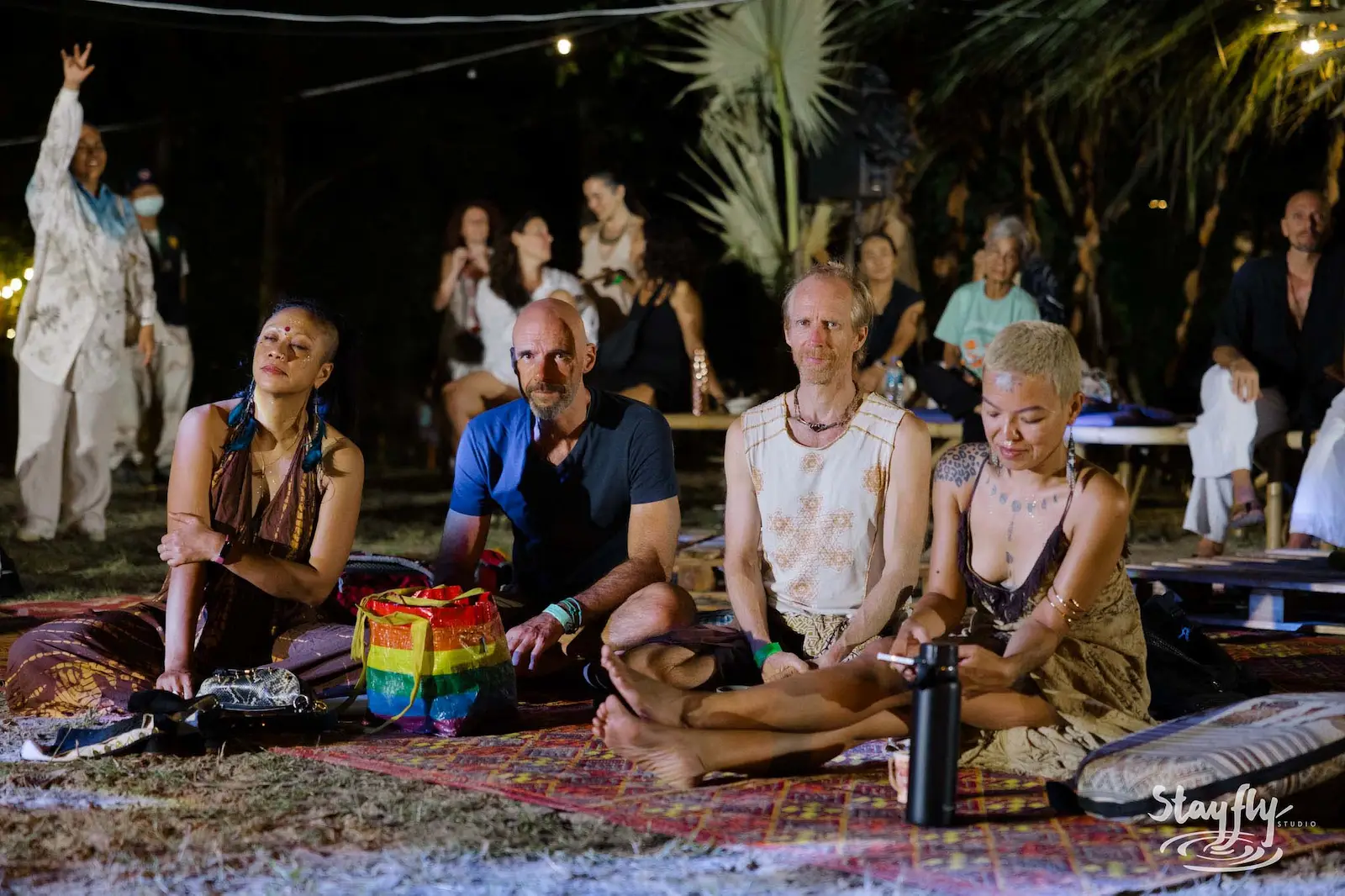 Four people seated cross-legged at night gathering.