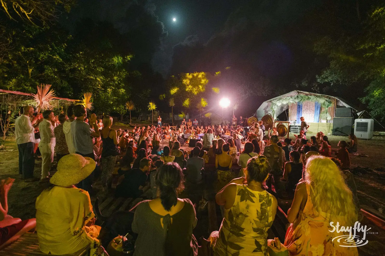 Large crowd gathered outdoors at night under moon.
