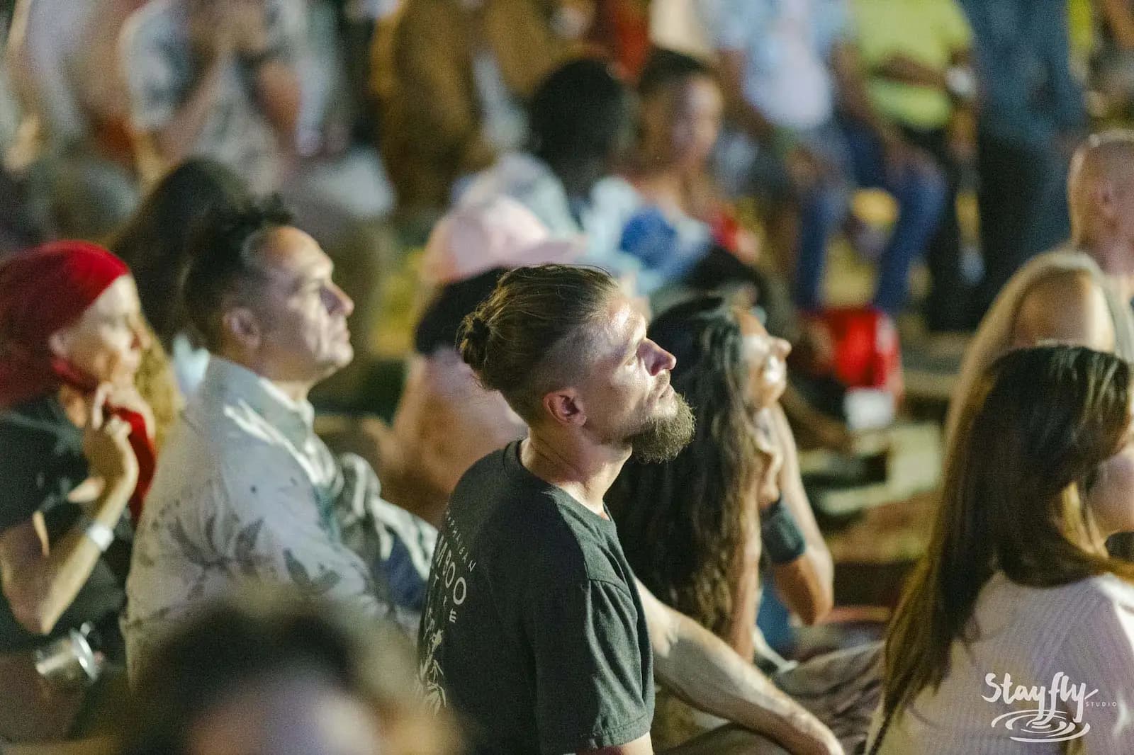 Audience faces gazing upward in warm dusk light.