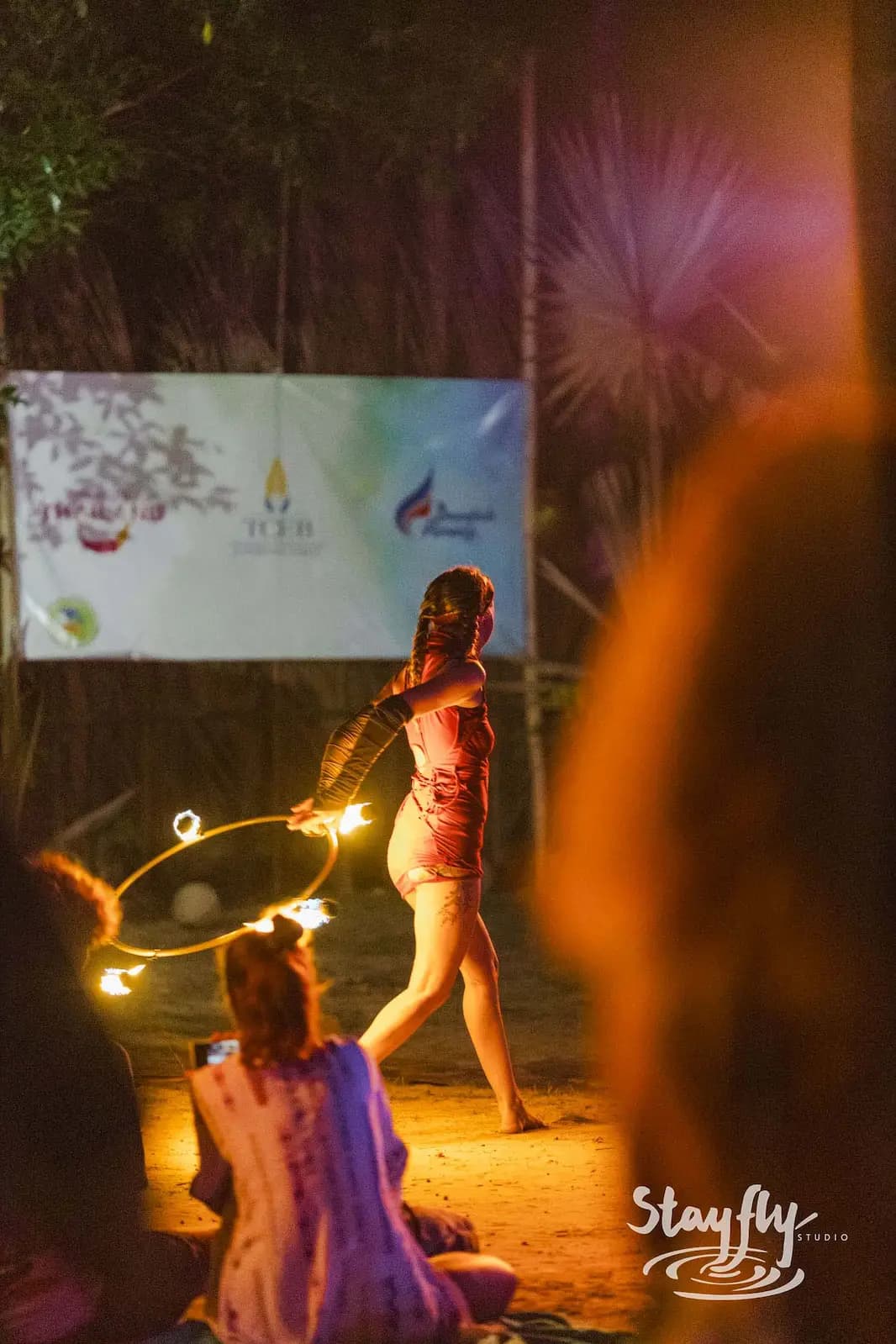 Fire hoop dancer performing at night for seated crowd.
