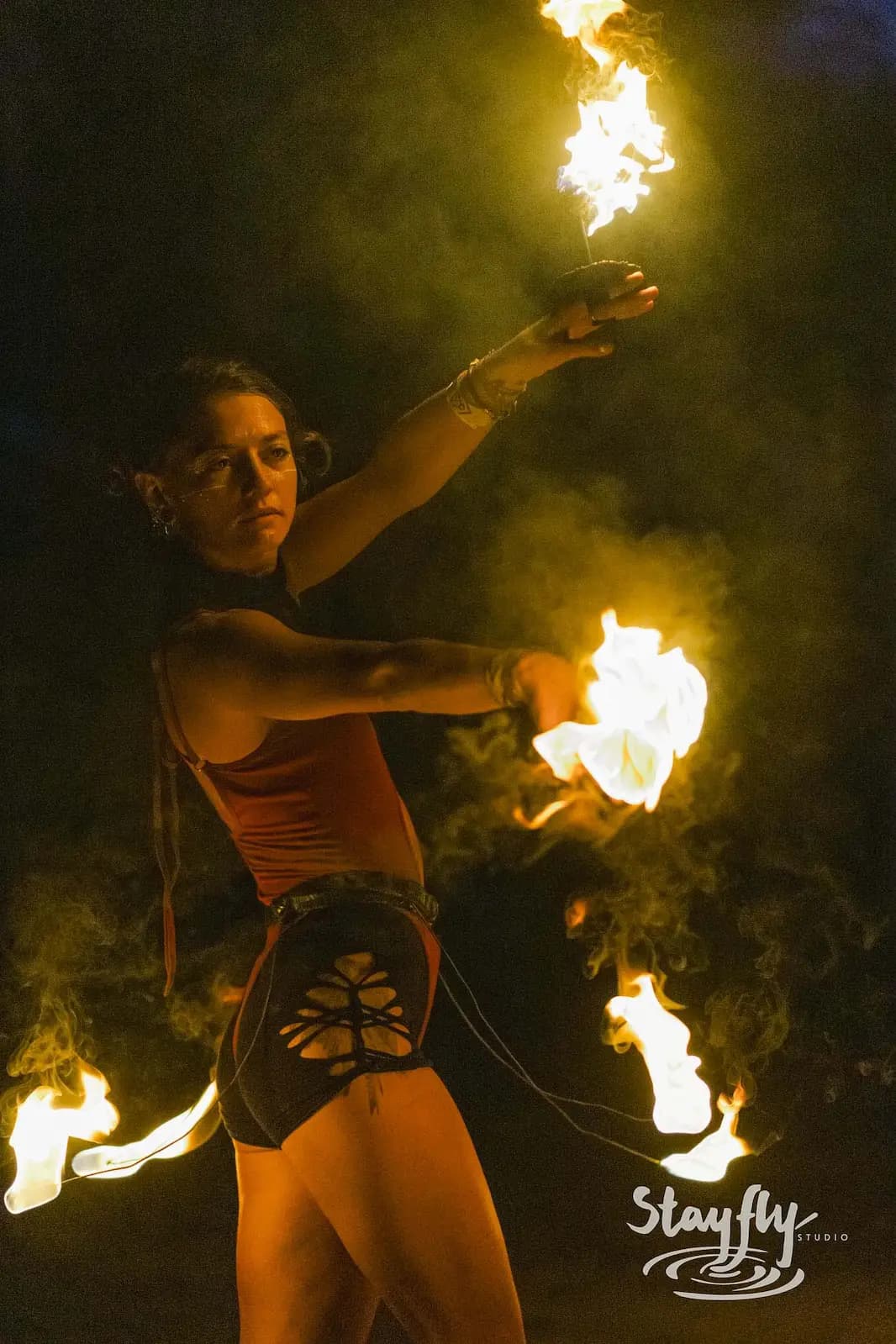 A performer spins flaming poi through drifting smoke at night.