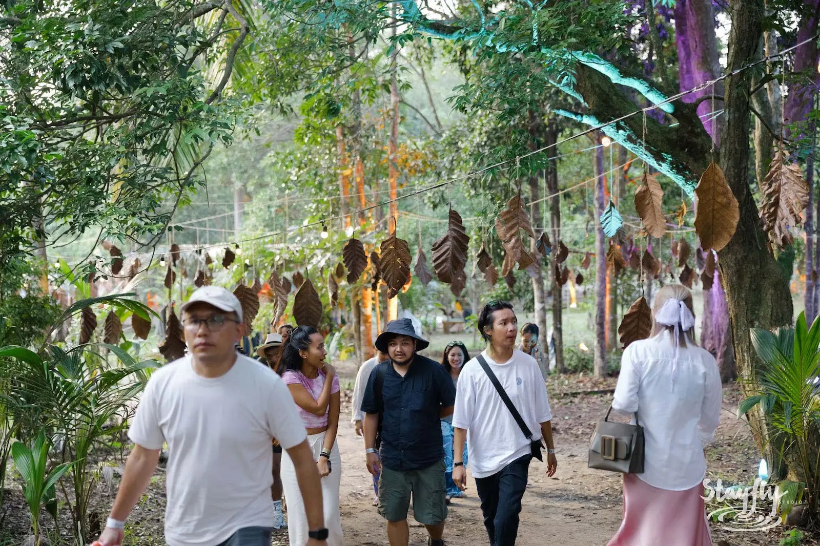 Attendees walking wooded path lined with hanging leaves.