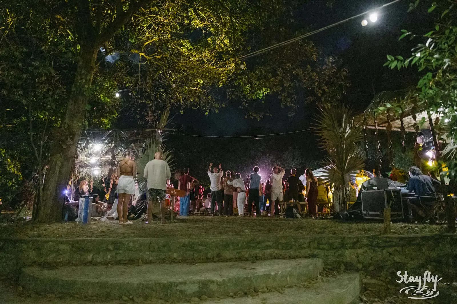People dancing at night near steps and trees.