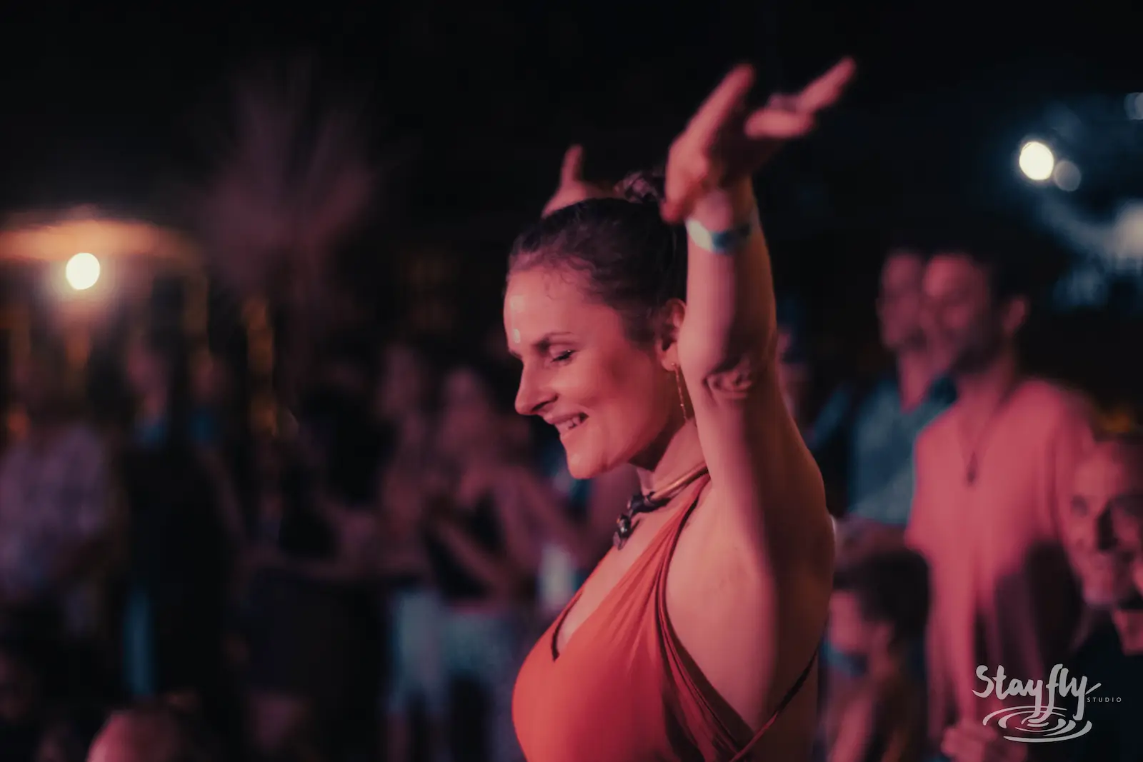 Woman dancing with hands raised under red light.
