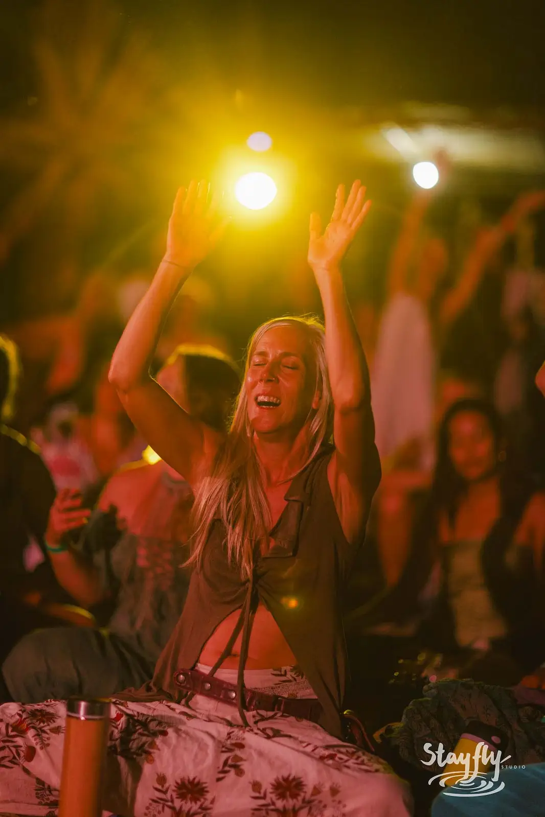Woman with raised arms dancing in night crowd.