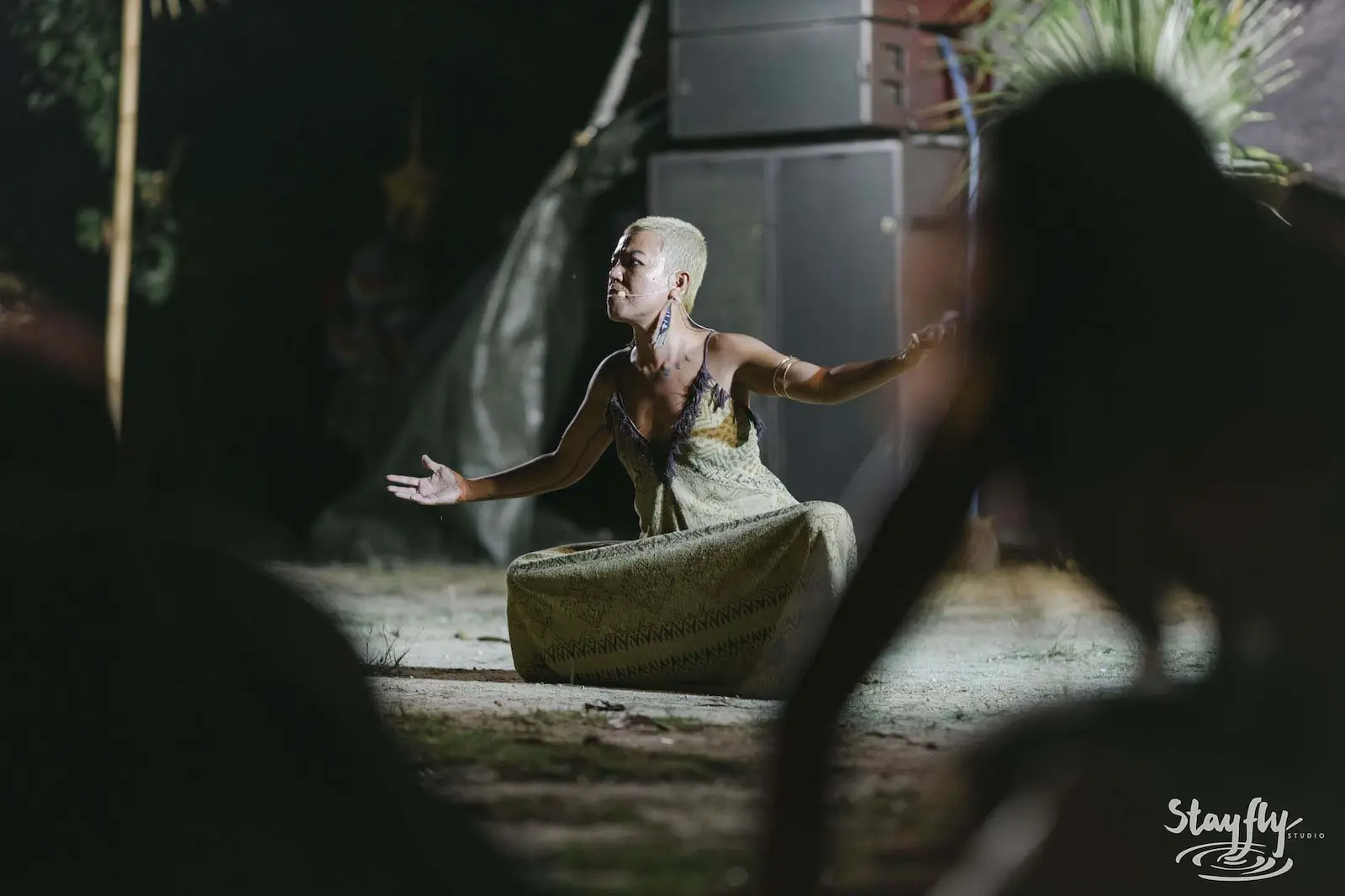 Bald woman crouched in dramatic dance pose at night.