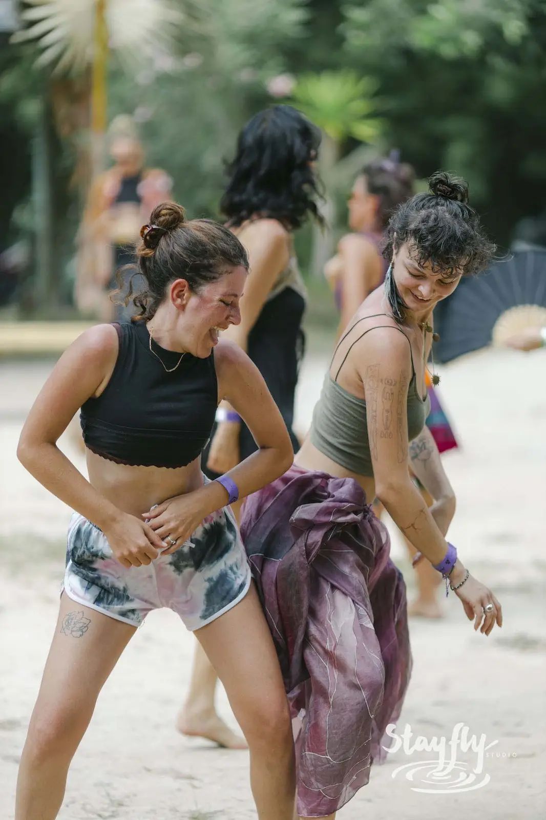 Two women dancing on sand in daylight.