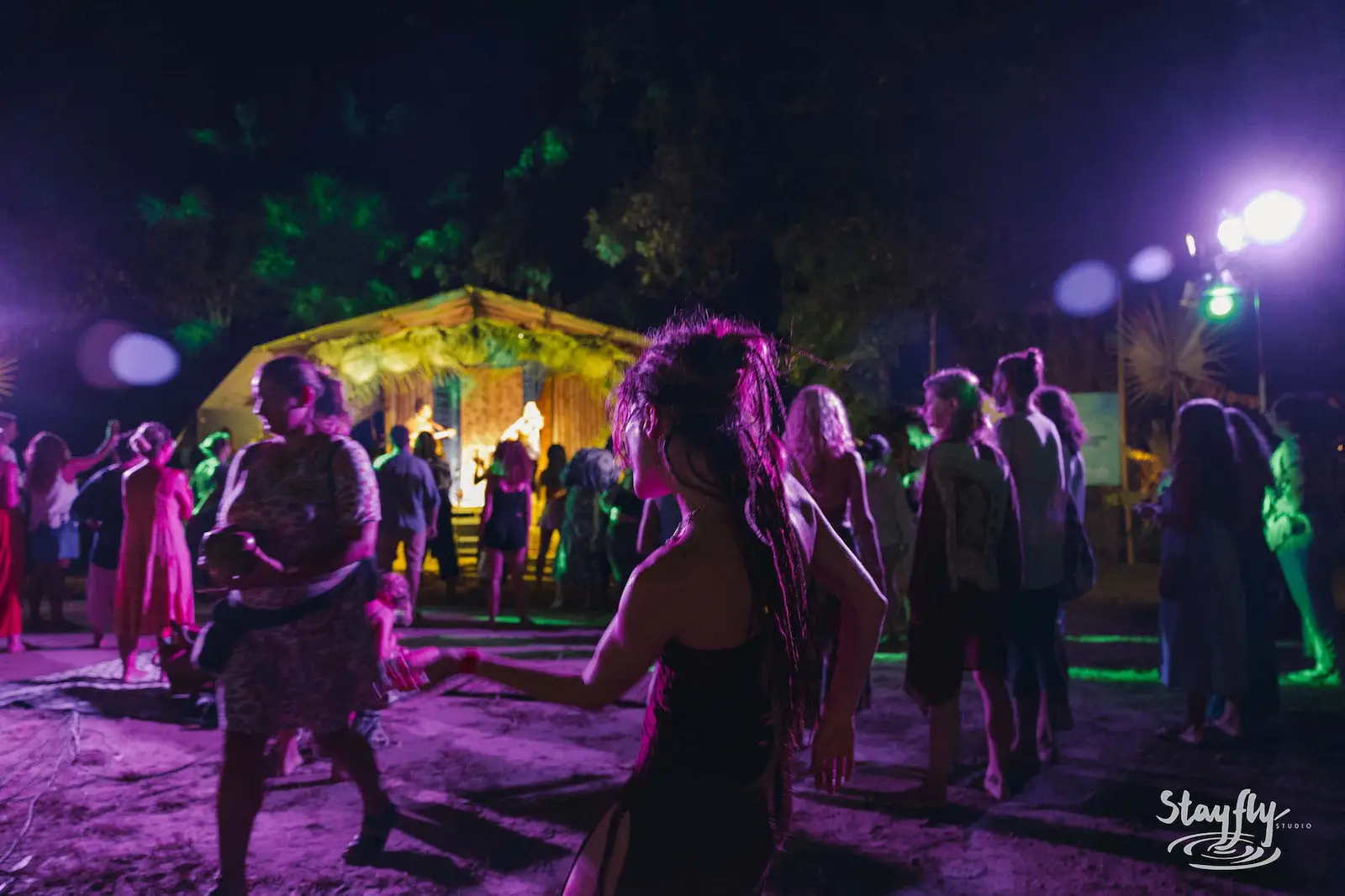 Crowd dancing near lit tent at night.