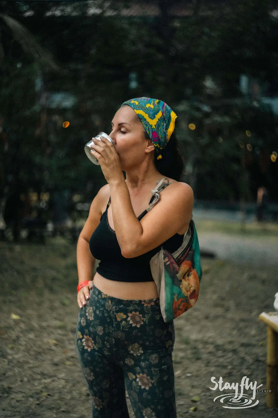 Woman in headwrap drinks from cup outdoors.