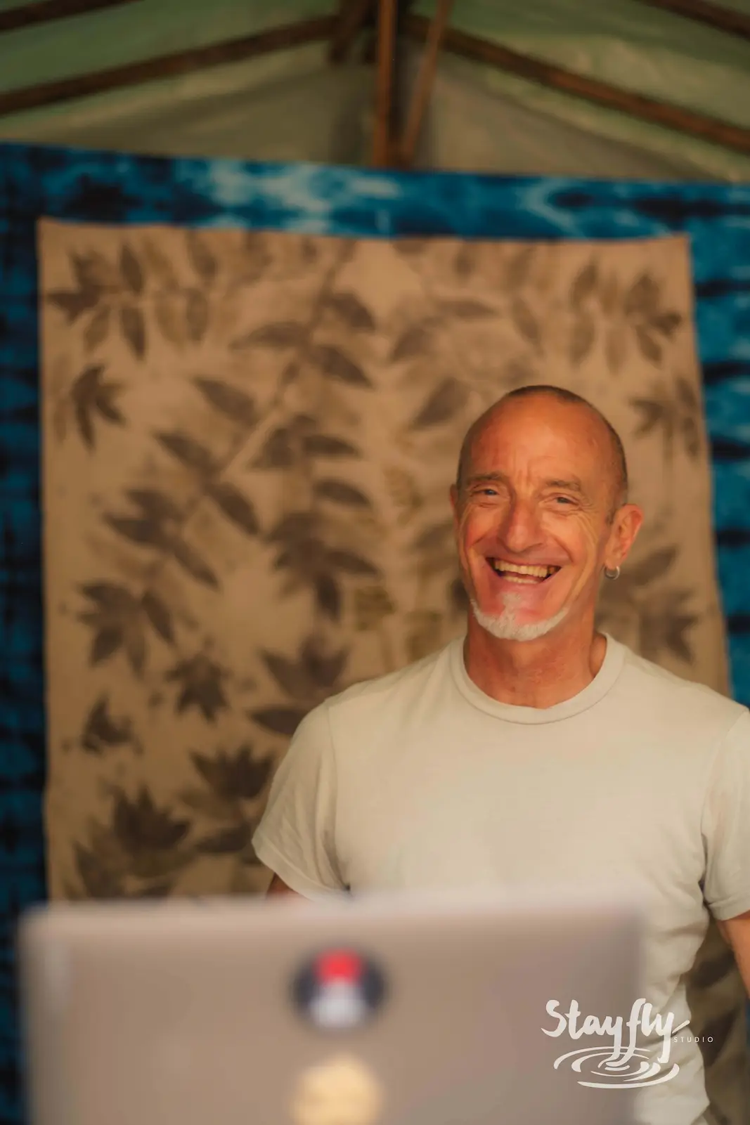Man laughing behind laptop under tent canopy.