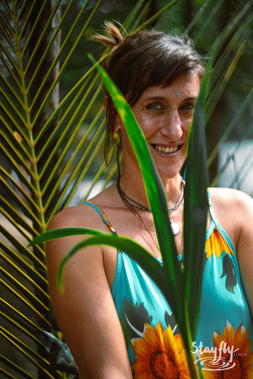 Woman smiling behind palm frond, sunflower top.