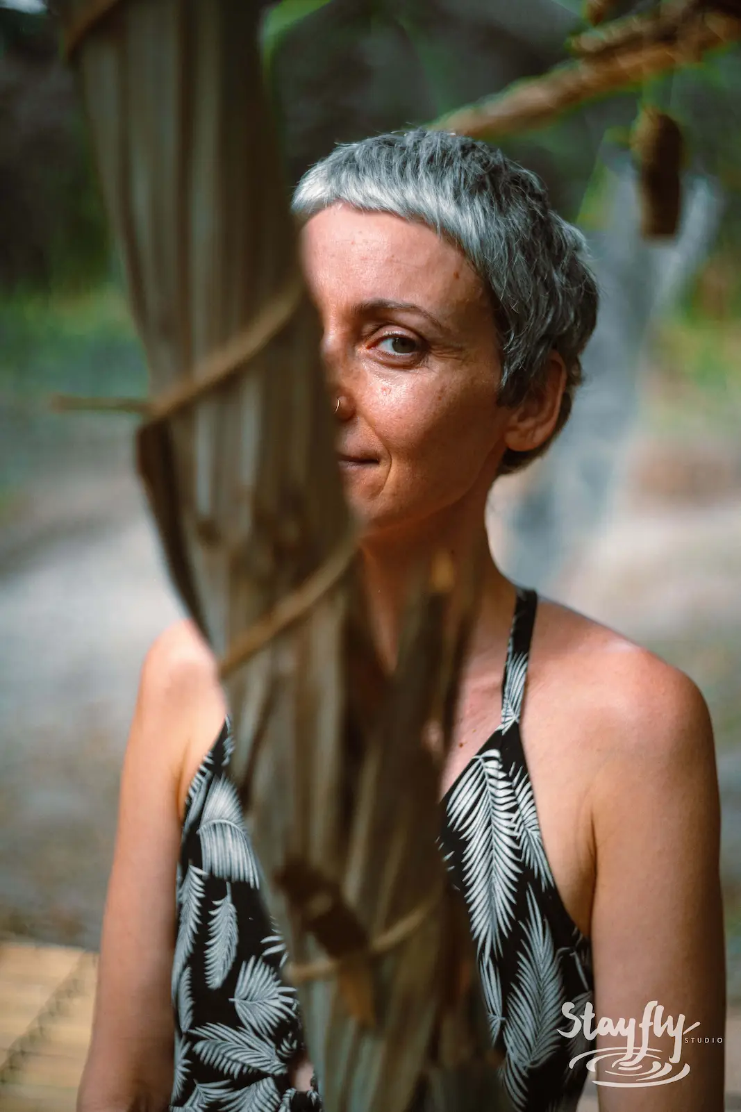 Woman with grey hair partly hidden behind tree branch.