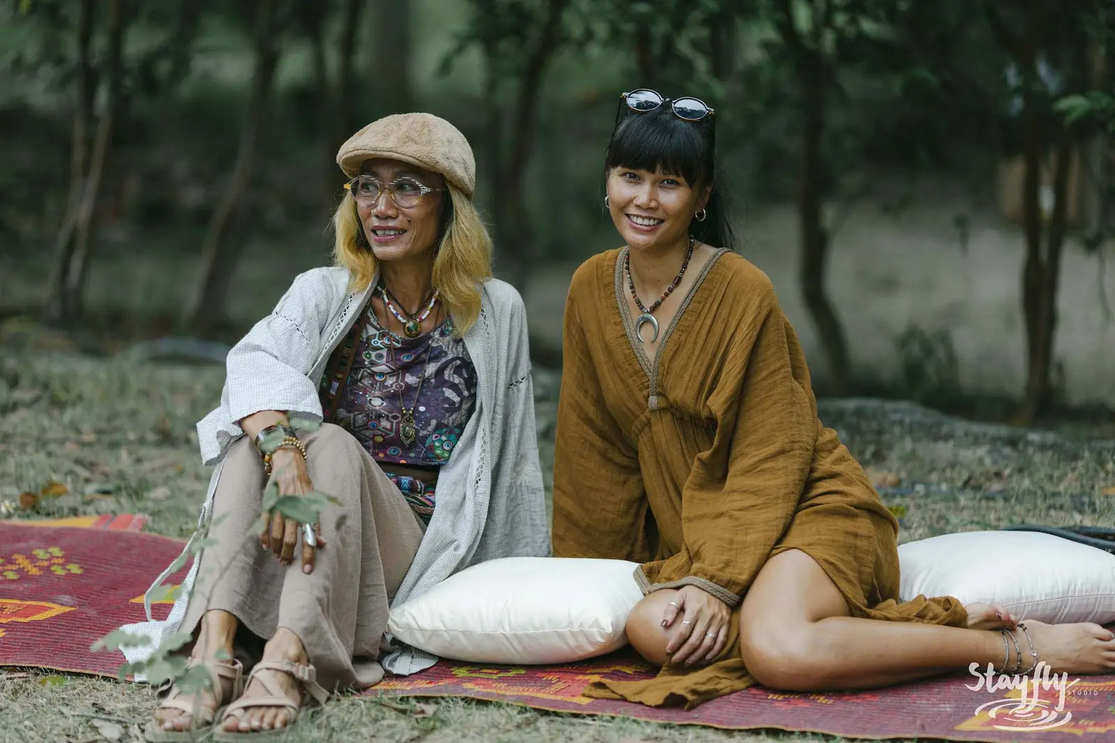 Two women sitting on a rug smiling together.