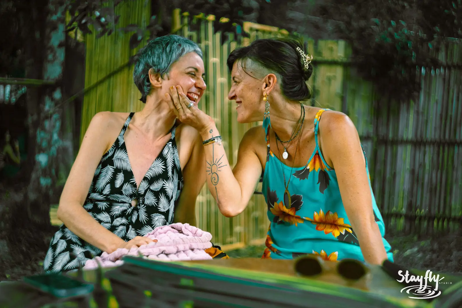 Two women laughing together by decorated fence.