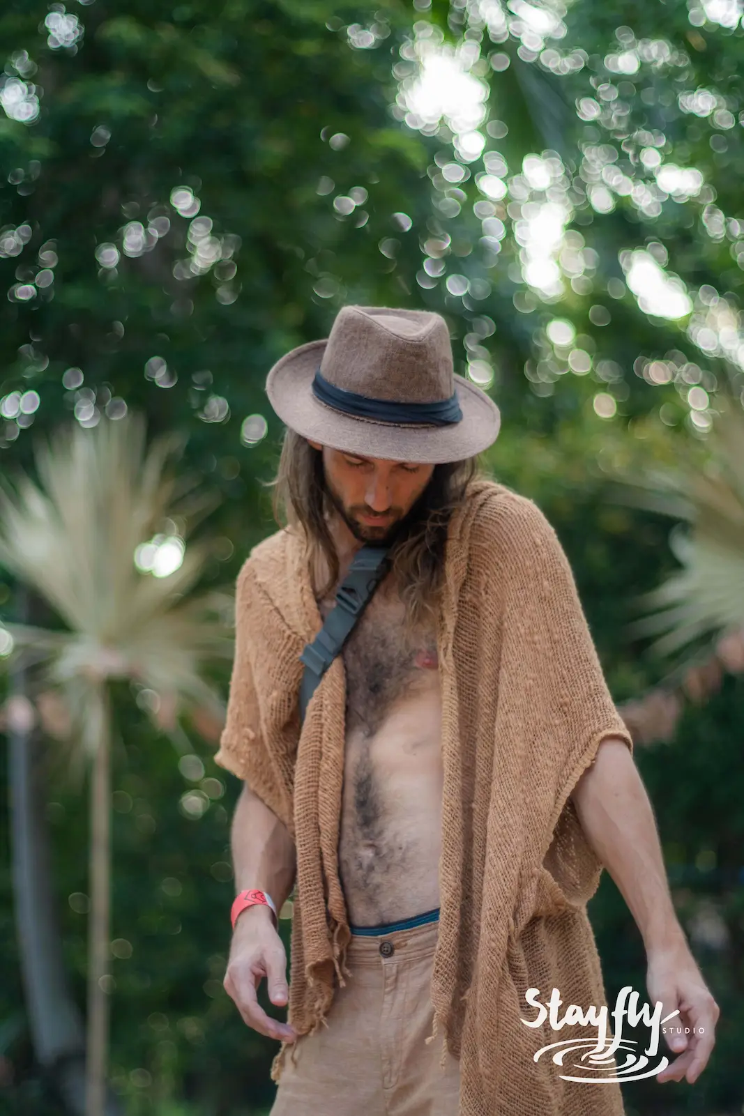 Man in tan poncho and hat among trees.