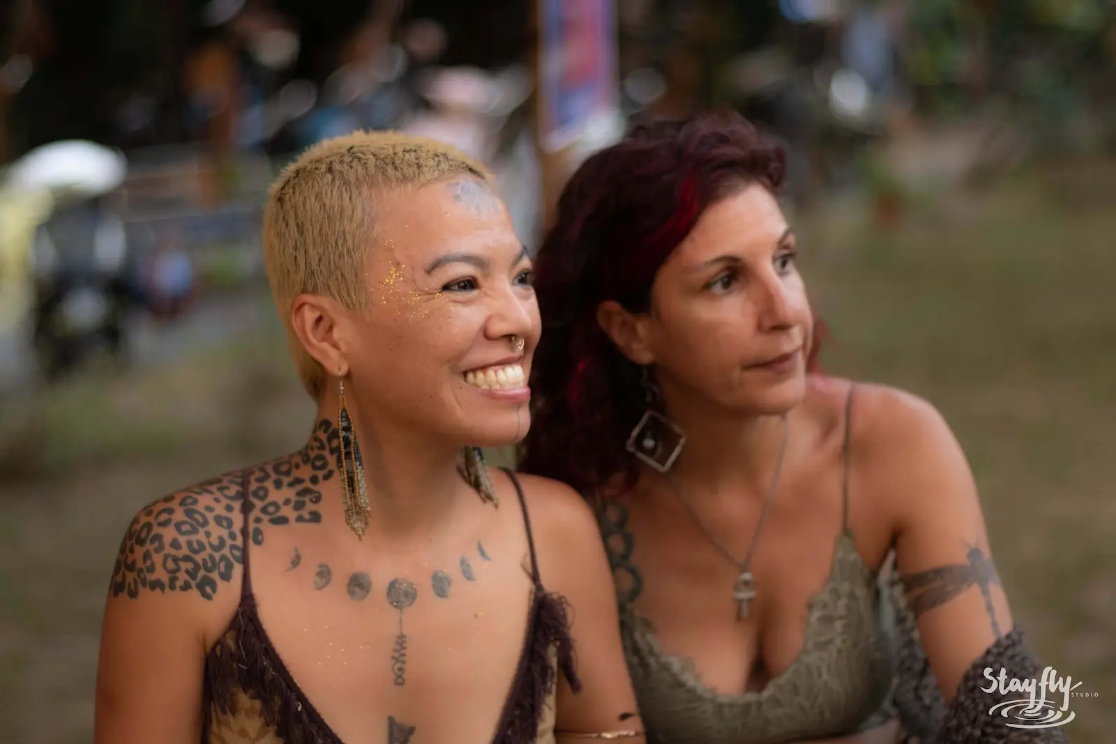 Two women smiling together, tattoos visible.