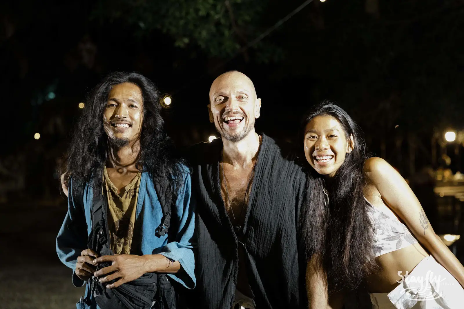 Three people smiling together at night.