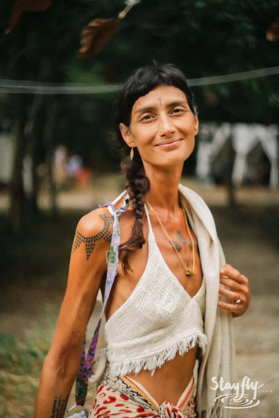 Woman smiling with shoulder tattoo and necklaces.