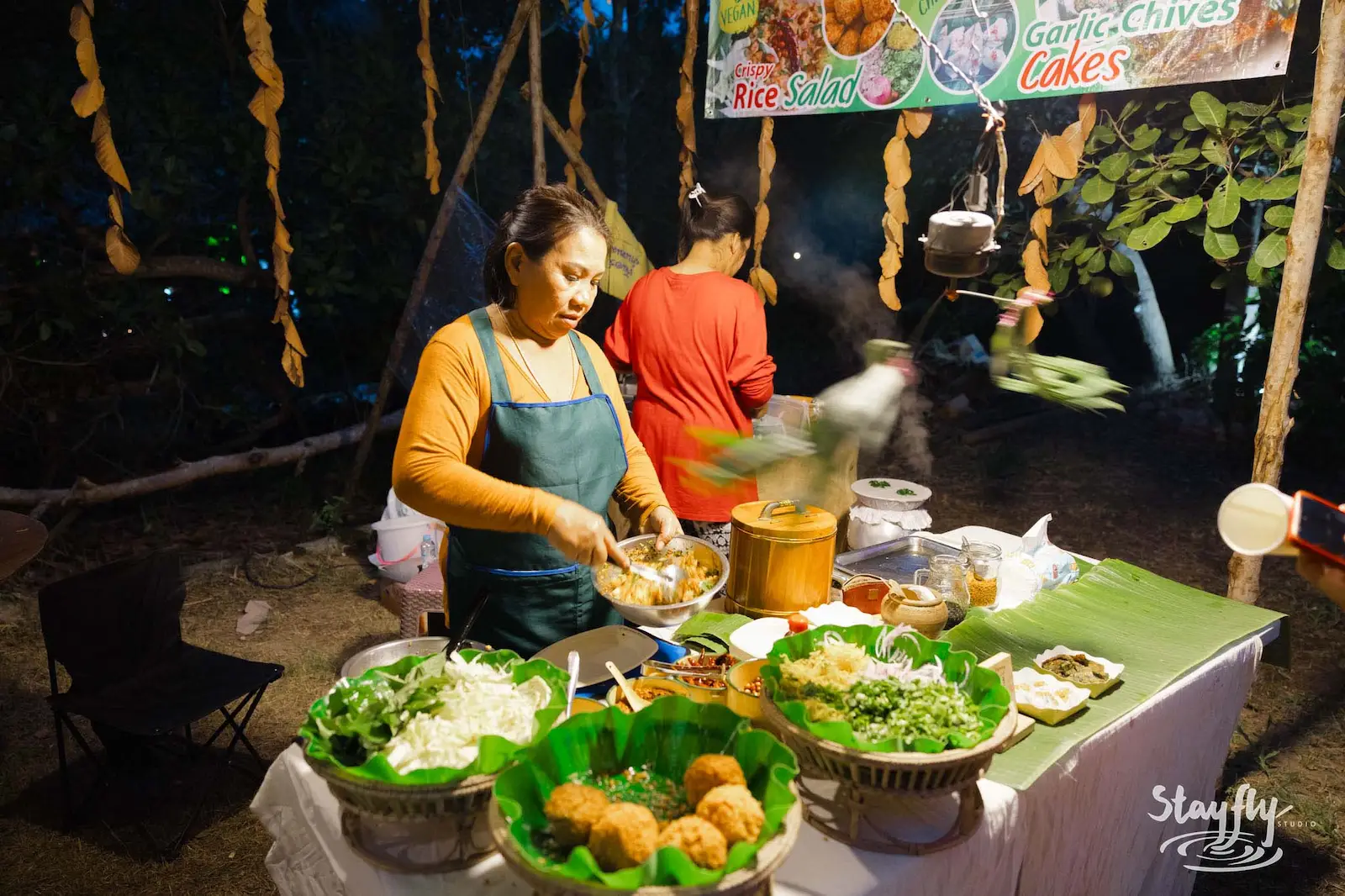 Woman cooks at night food stall with menu signs.