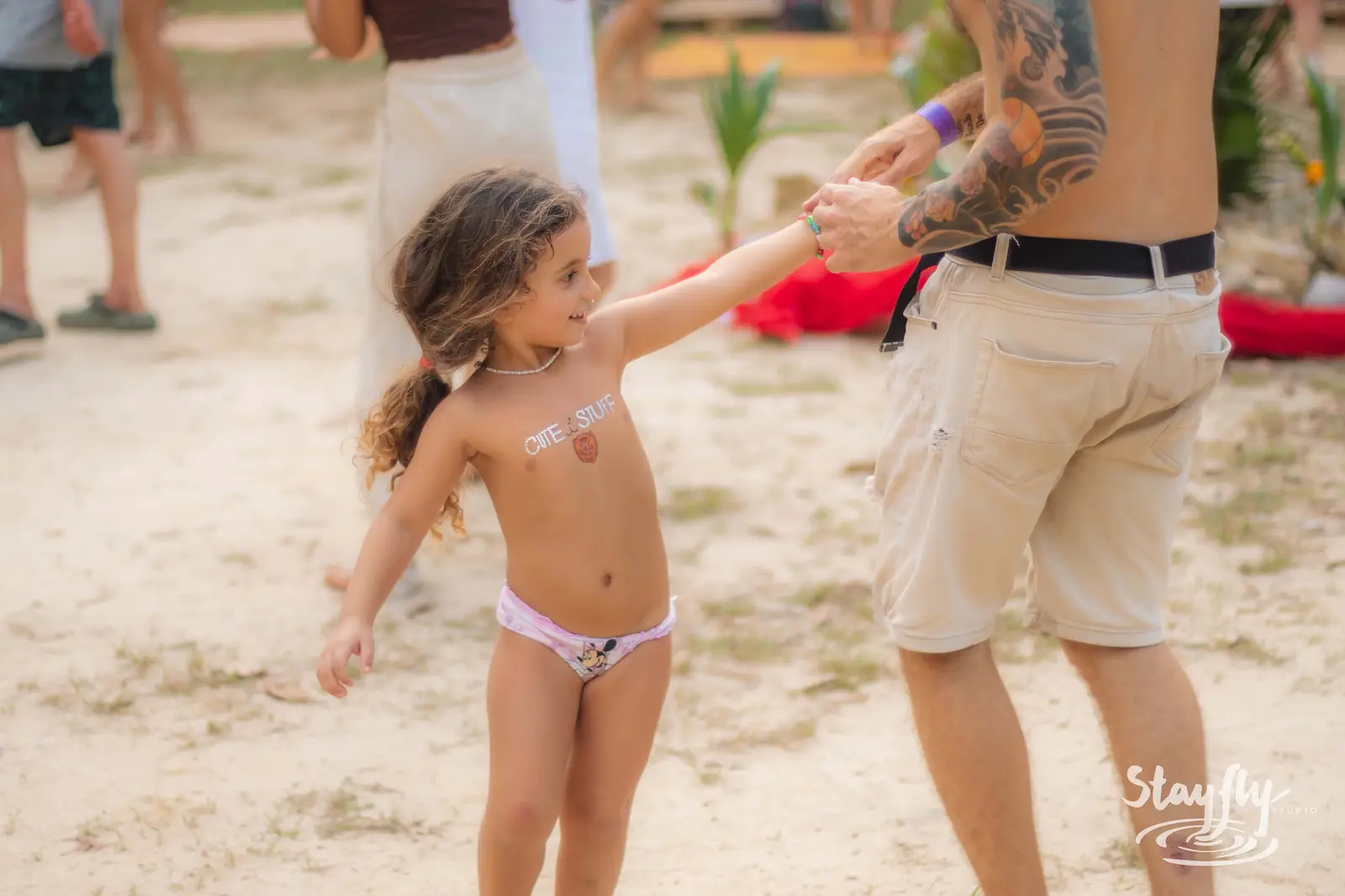 Child dancing hand in hand with adult on sand.