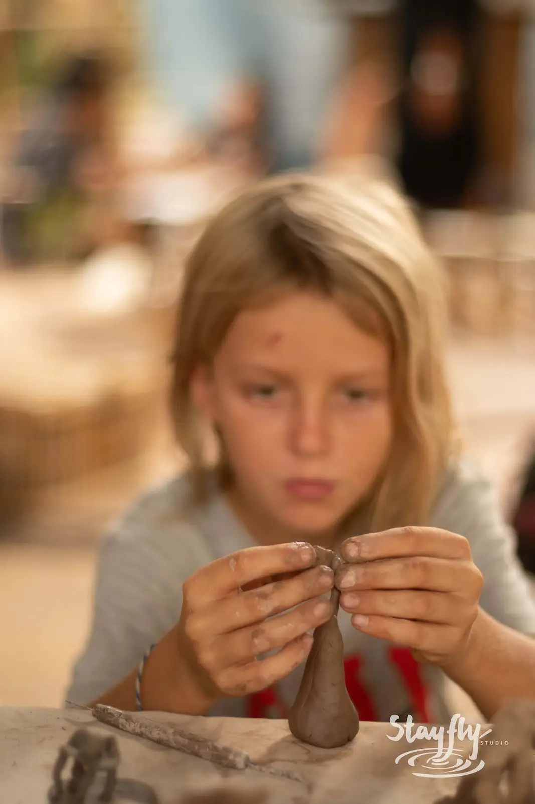 Child shaping clay with hands at workshop table.