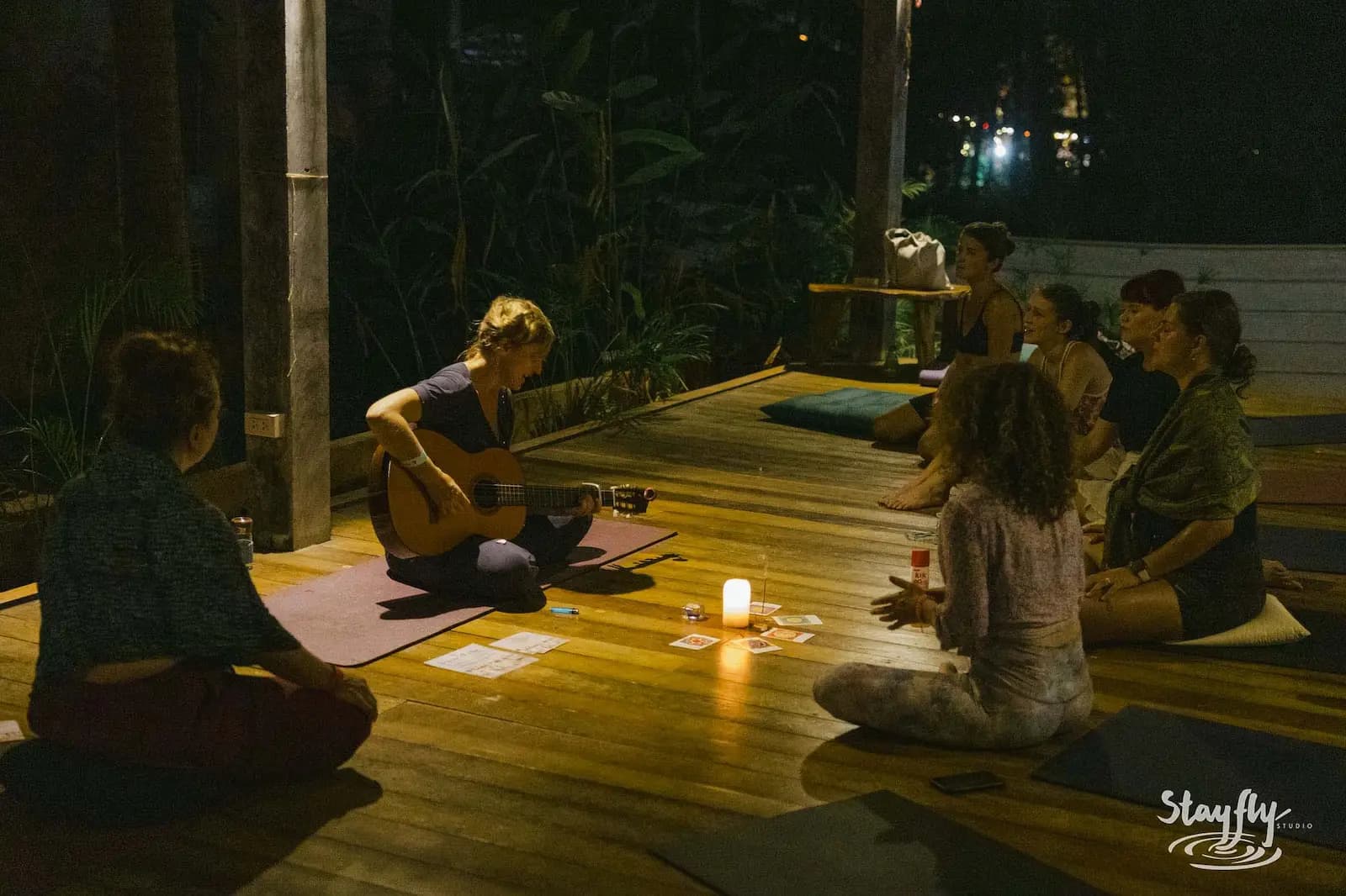 Woman playing guitar in candlelit evening circle.