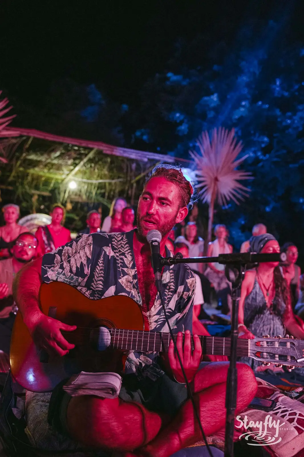 Man singing and playing guitar under colored stage lights.