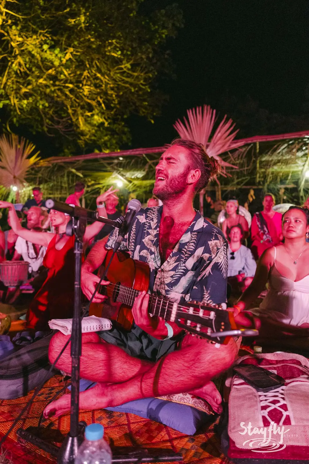 Man singing and playing guitar cross-legged at night.