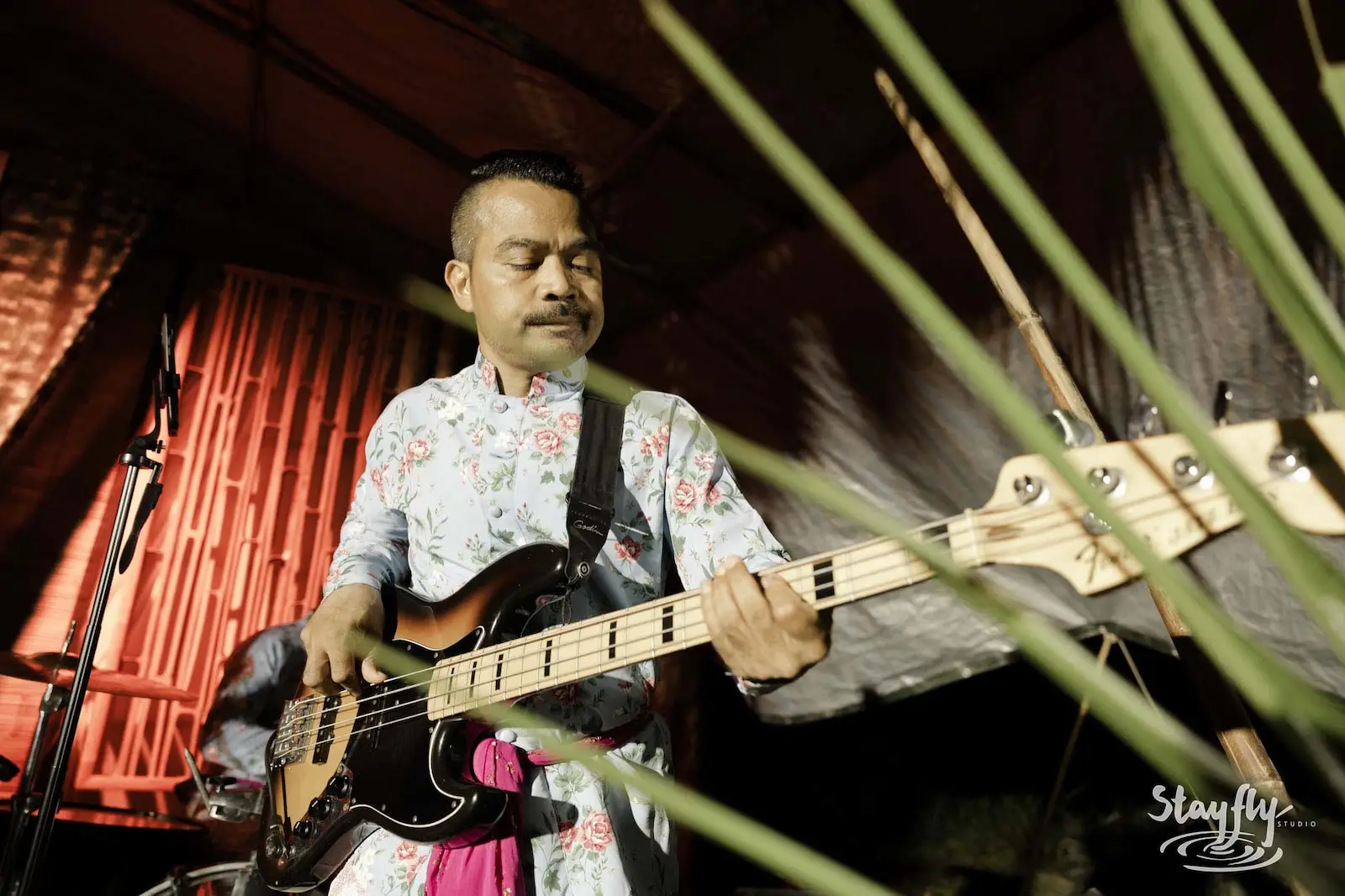 Bassist performing in floral shirt on stage.