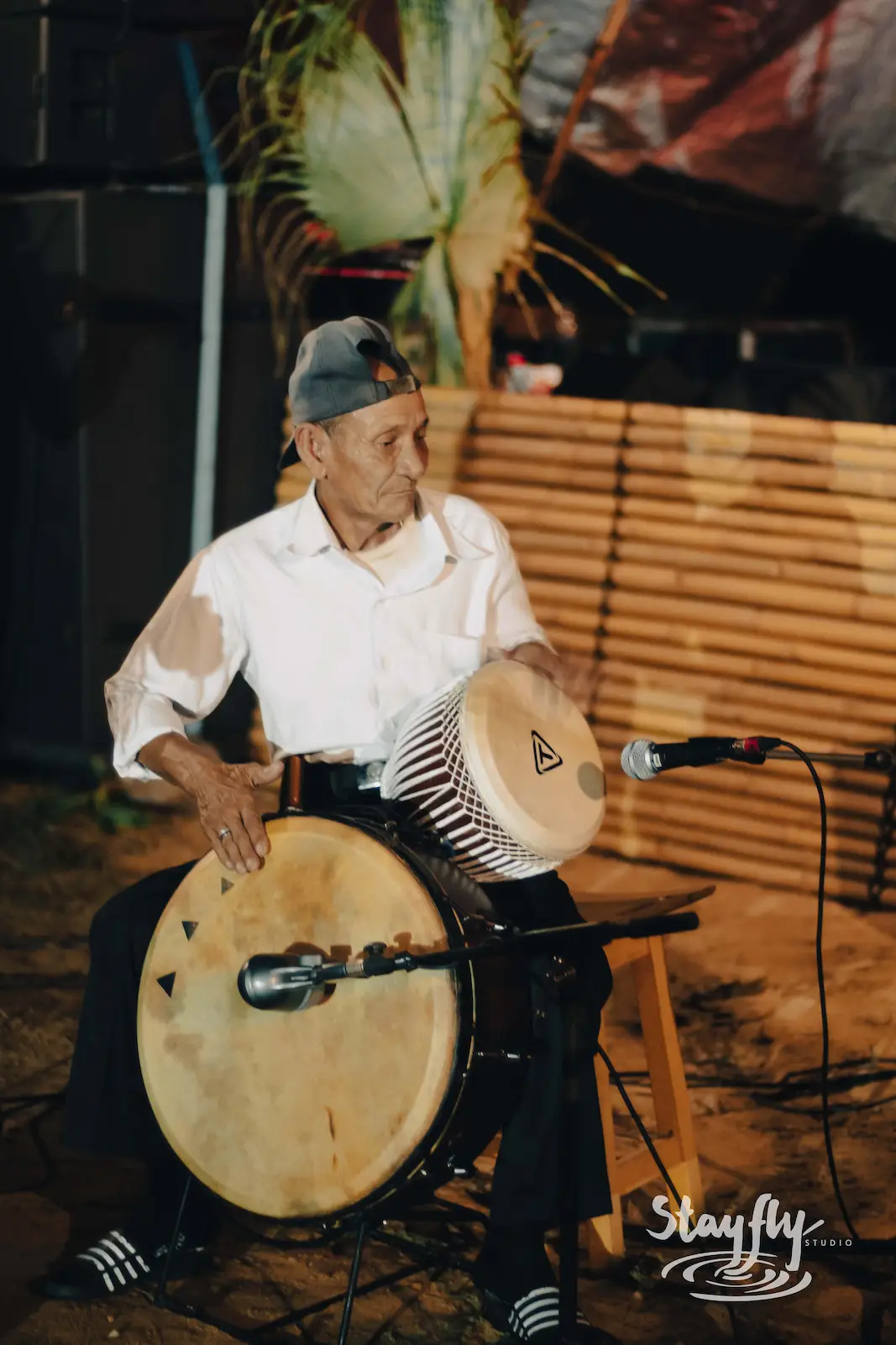 Elderly man playing frame drum on stage.