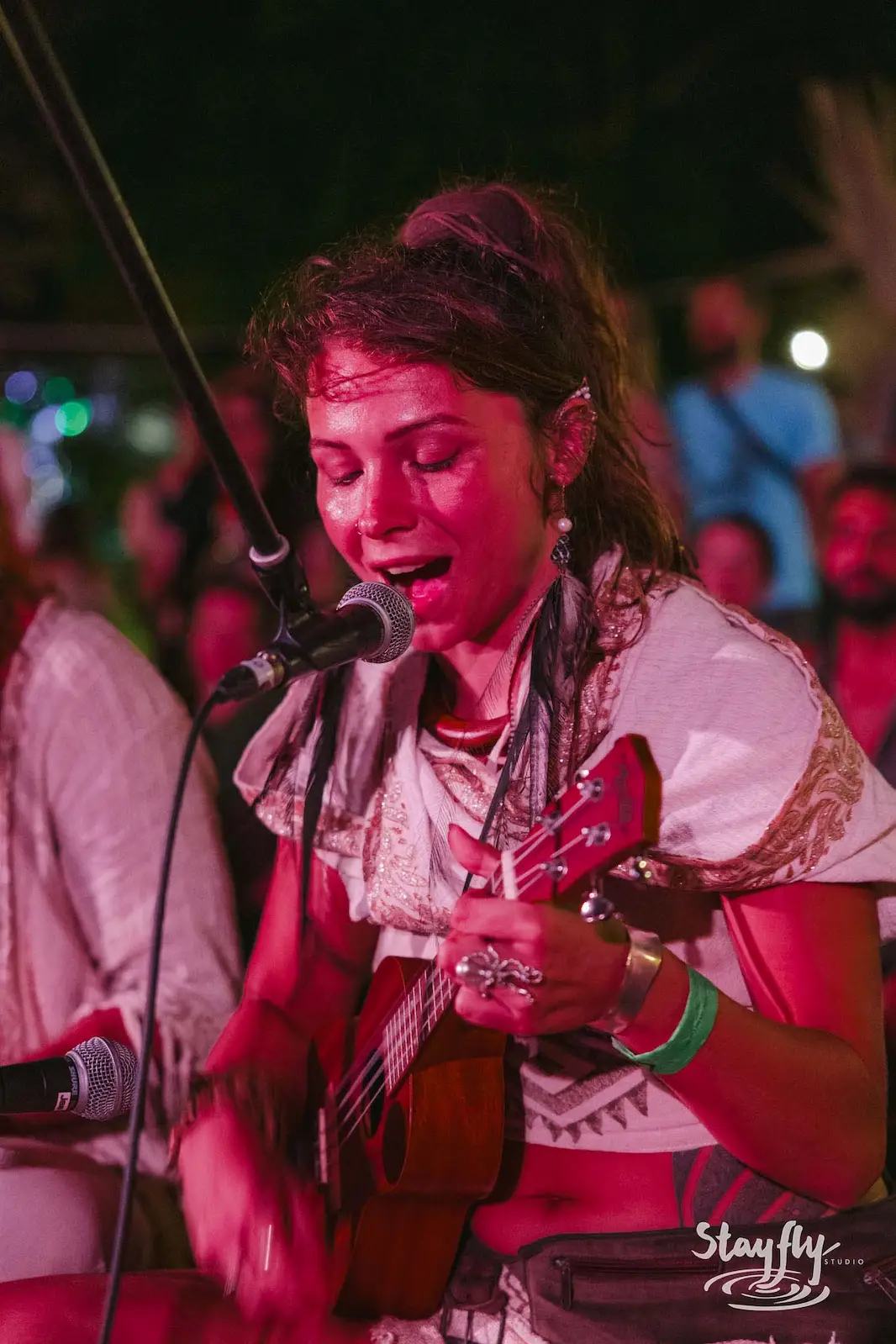 Woman singing into microphone with ukulele at night.