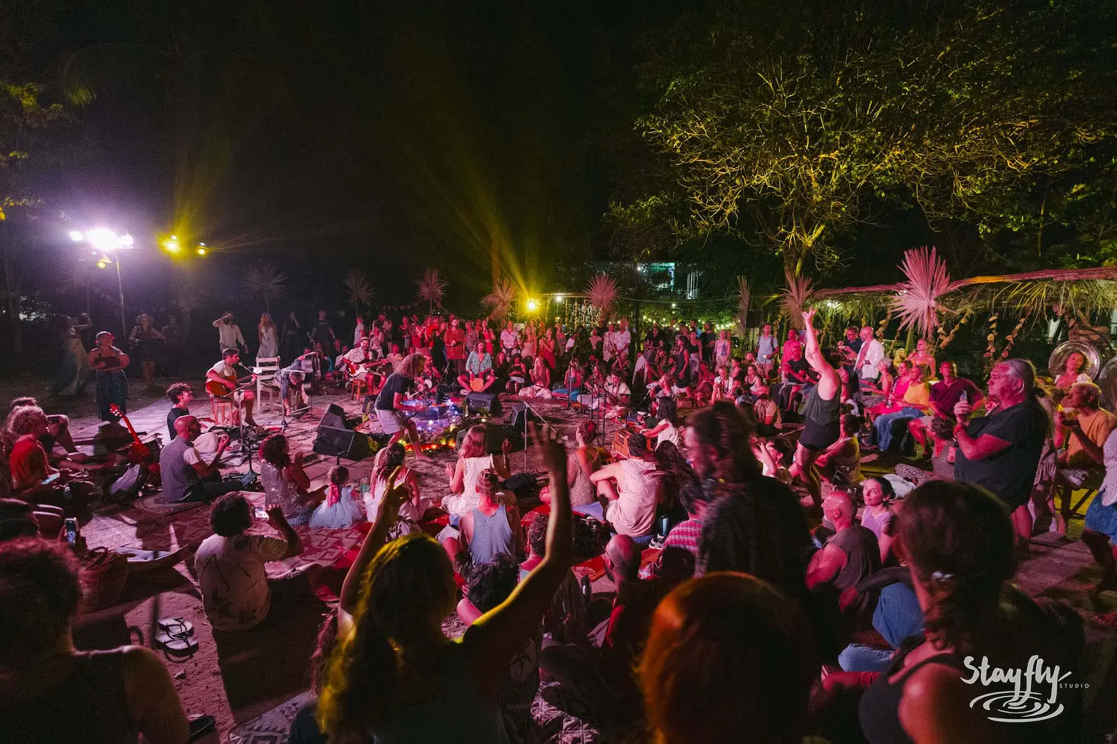 Crowd seated around fire-lit night stage listening to music.