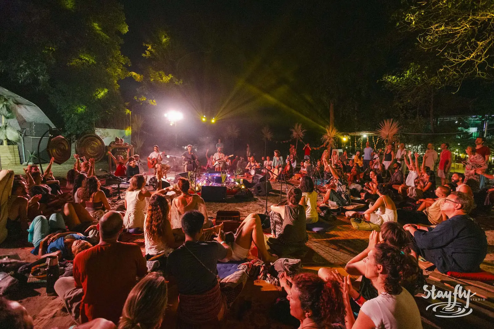 Musicians and dancers with arms raised at night circle.
