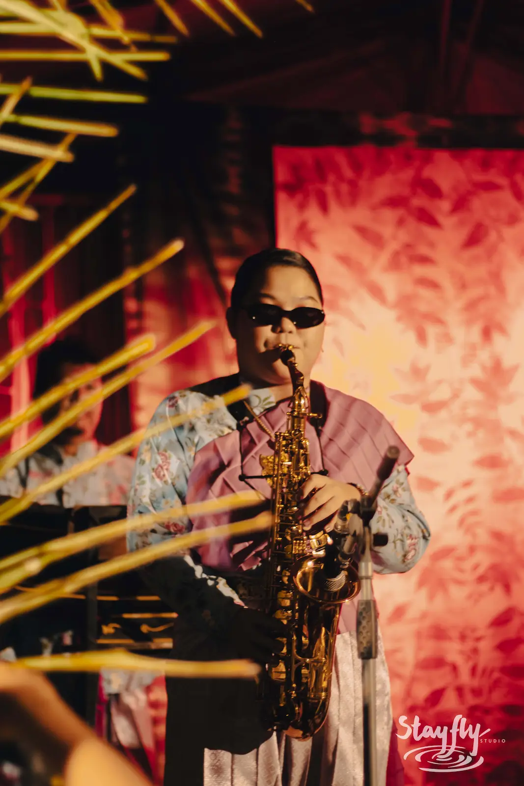 Saxophonist performing under red stage lighting.
