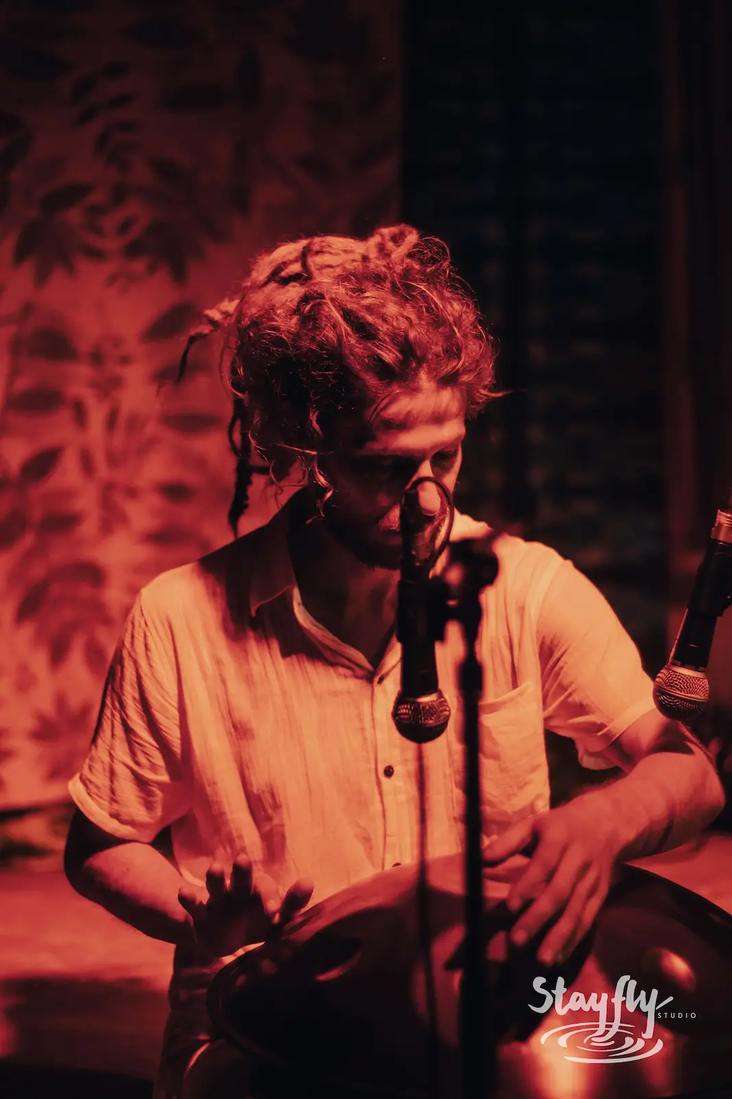 Dreadlocked drummer performing under red light.