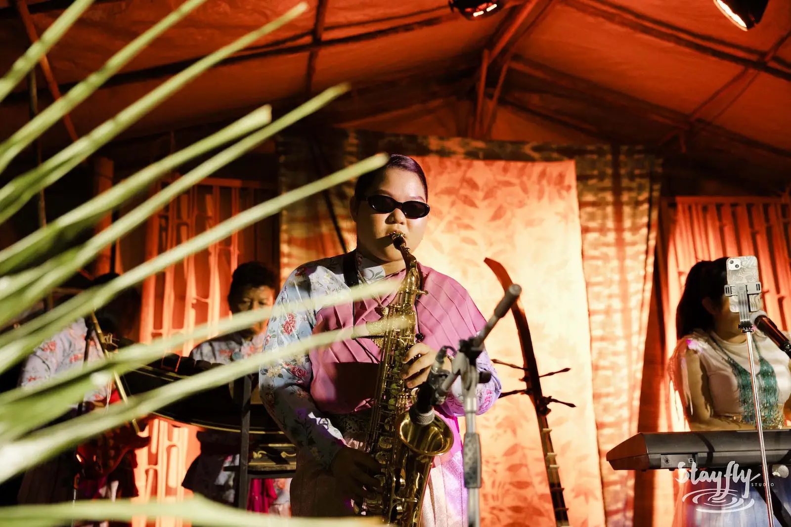 Saxophonist on night stage behind palm leaves.