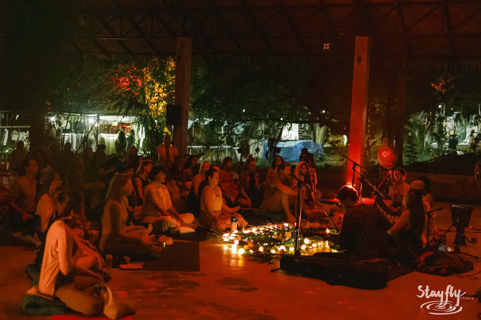 Seated crowd around candles listening to musicians at night.