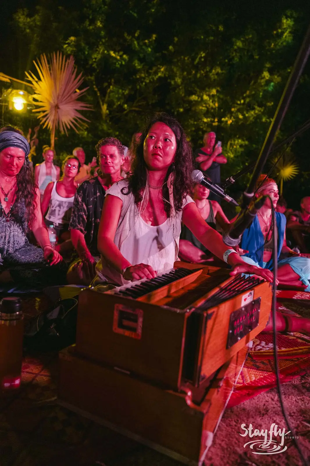 Woman playing harmonium with crowd gathered at night.