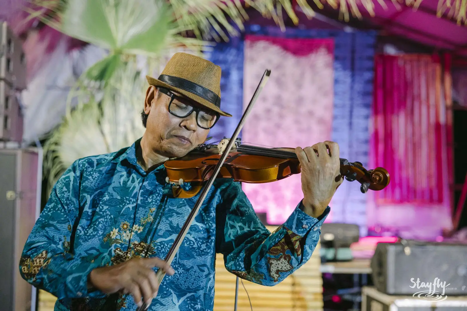 Violinist in hat under pink stage lighting.
