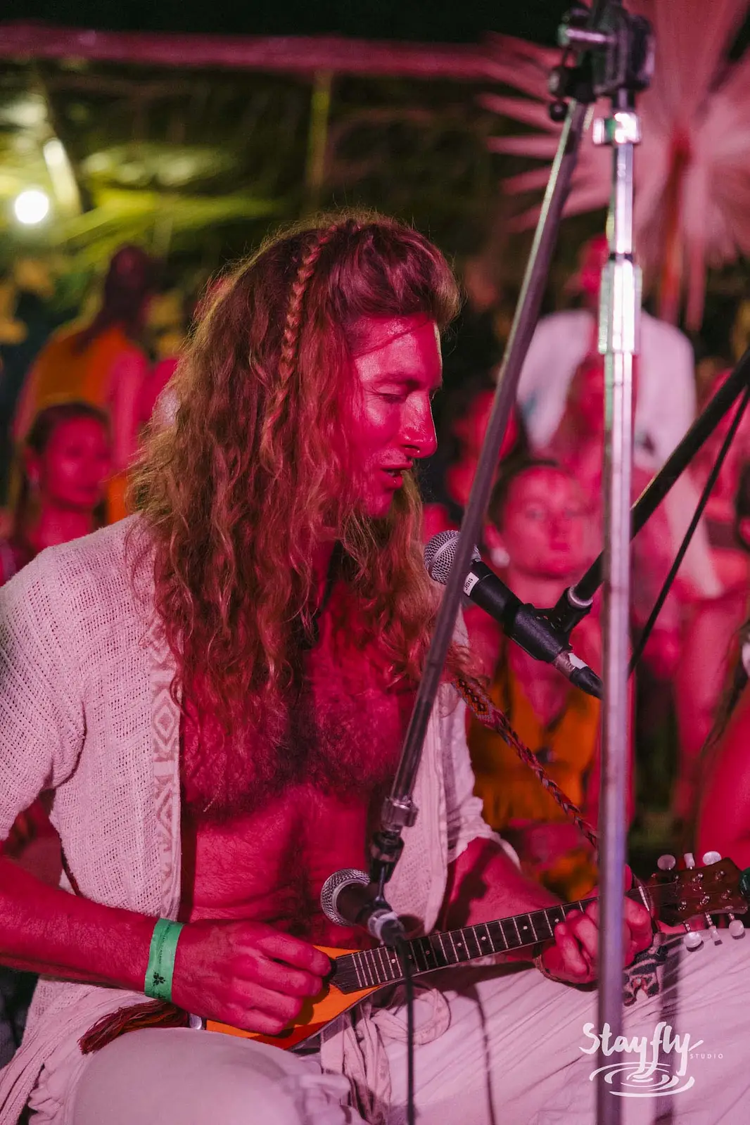 Musician with long hair playing stringed instrument, red light.