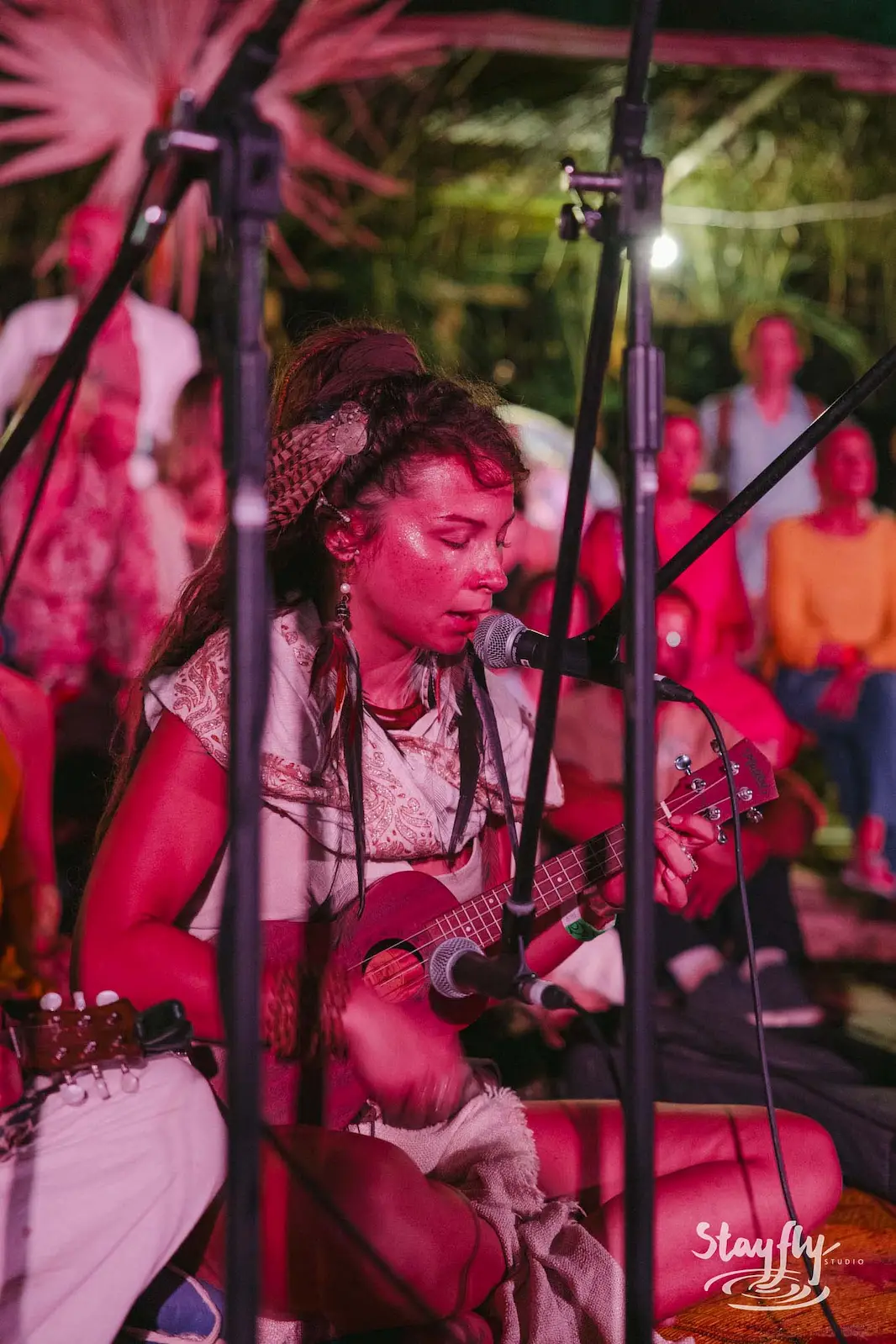 Woman singing and playing ukulele, crowd behind.