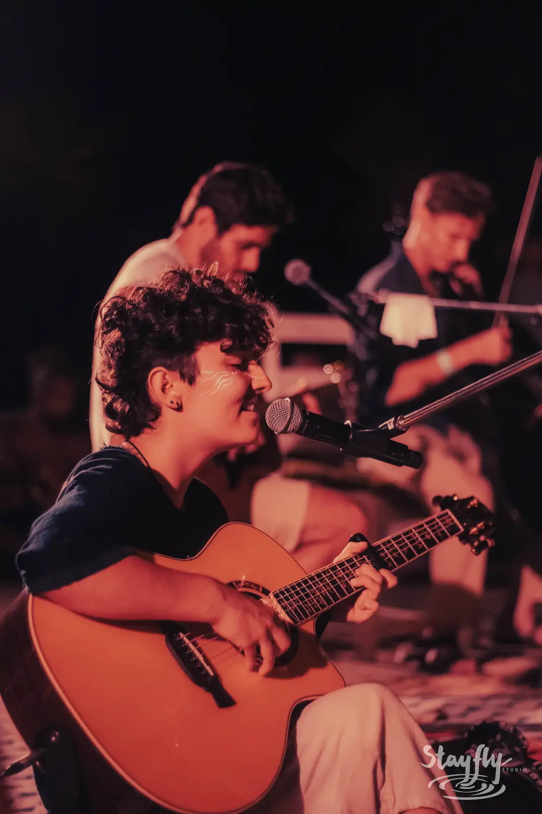 Young guitarist singing with bandmates behind.