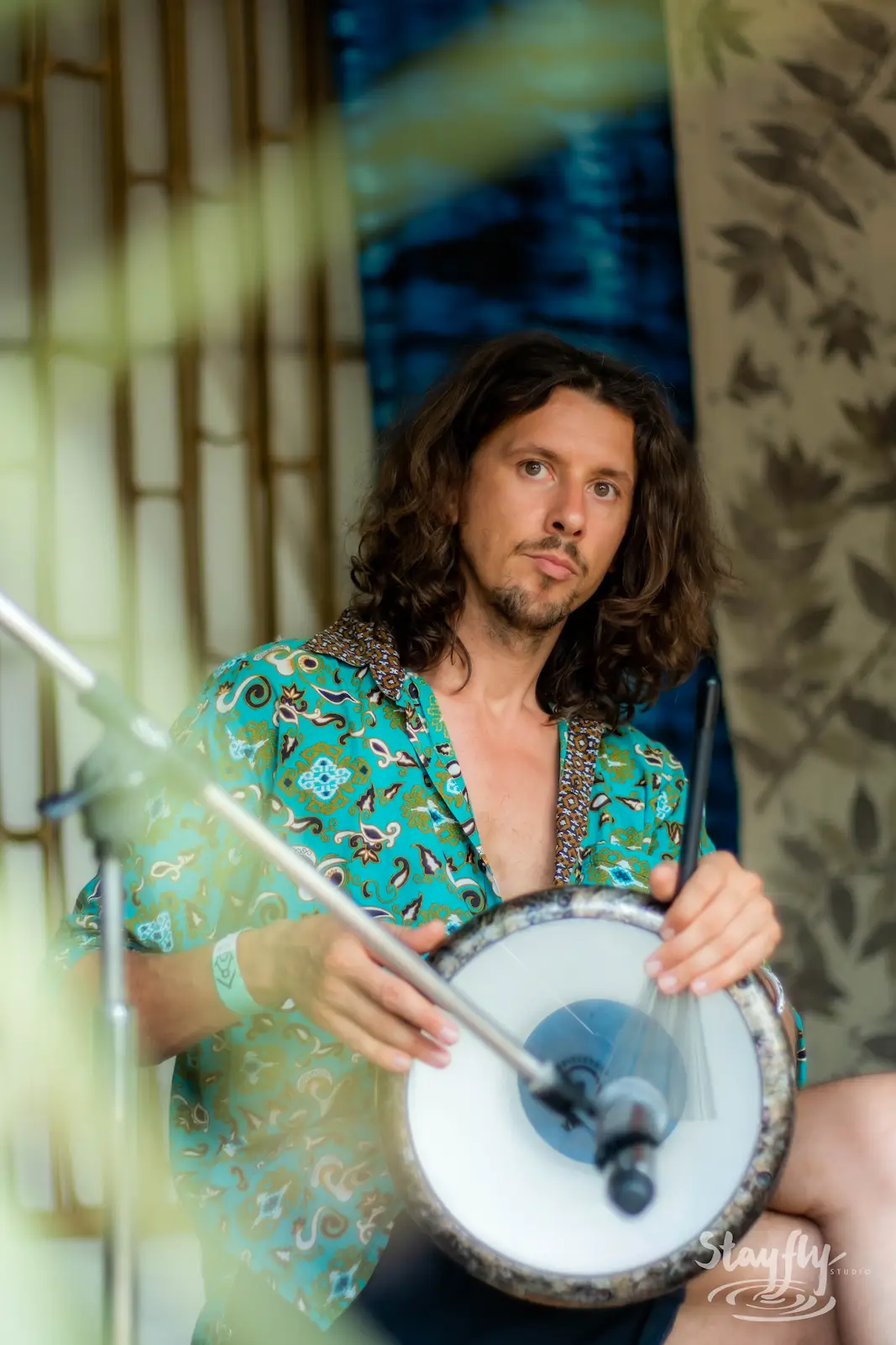 Drummer in patterned shirt playing hand drum.