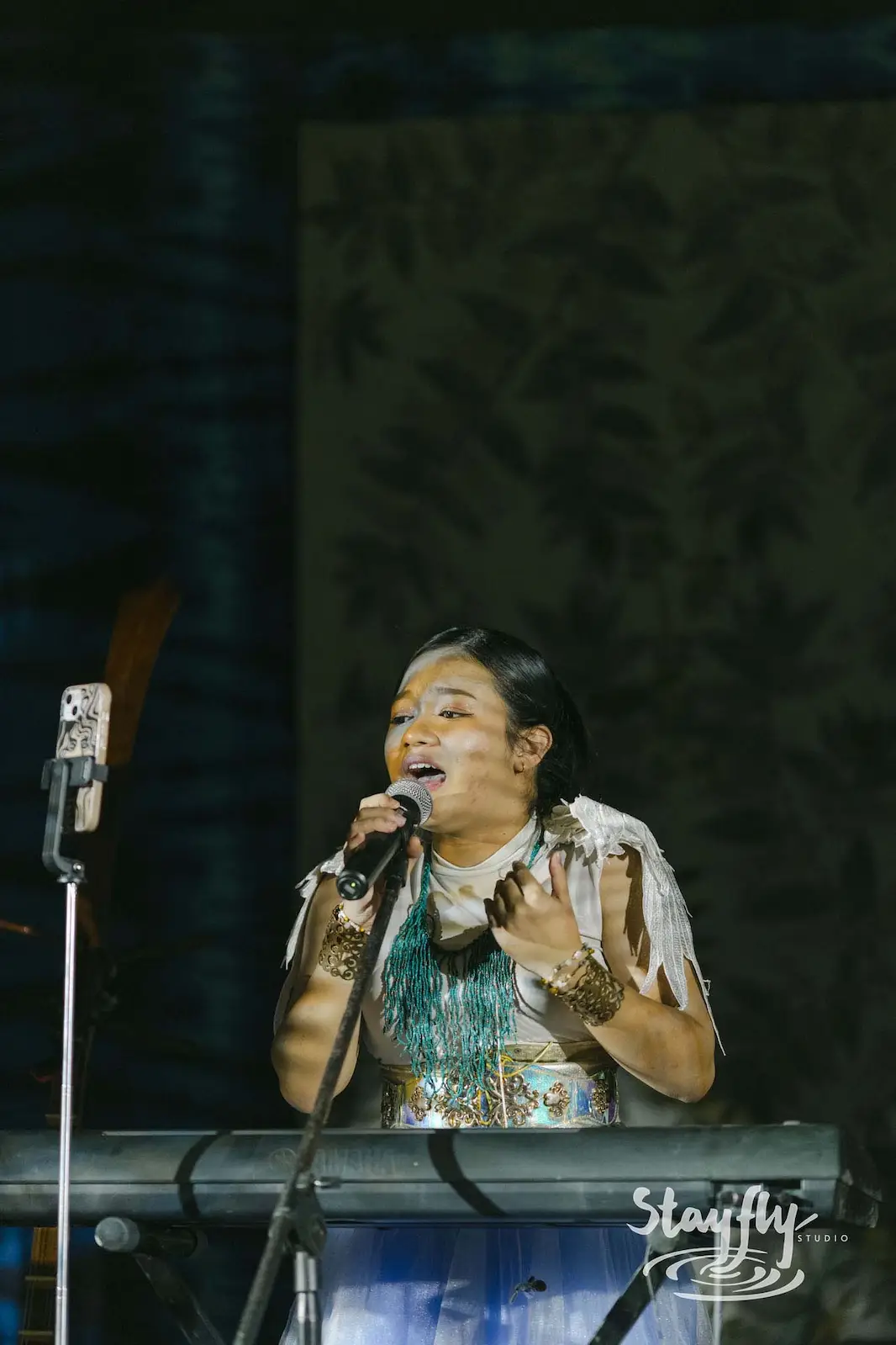 Singer performing at keyboard with beaded jewelry.