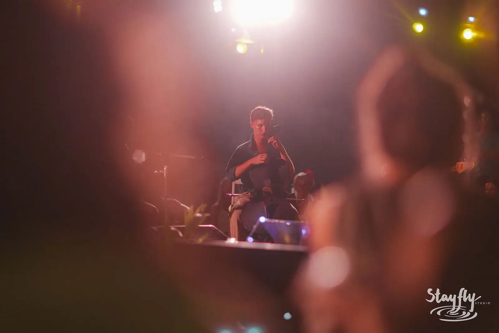 Musician on stage seen through blurred crowd hands.