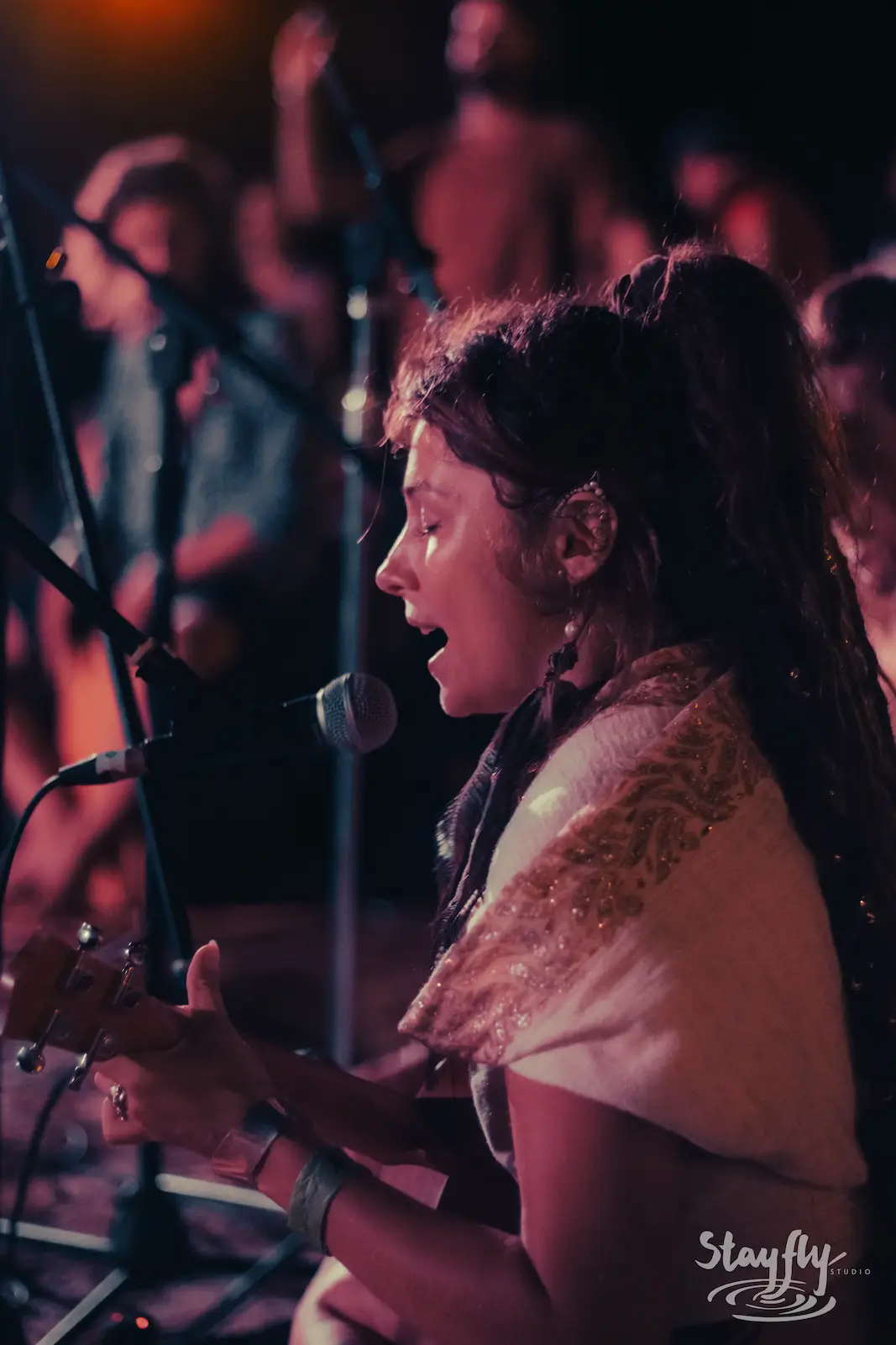 Woman singing with guitar at night, patterned scarf.