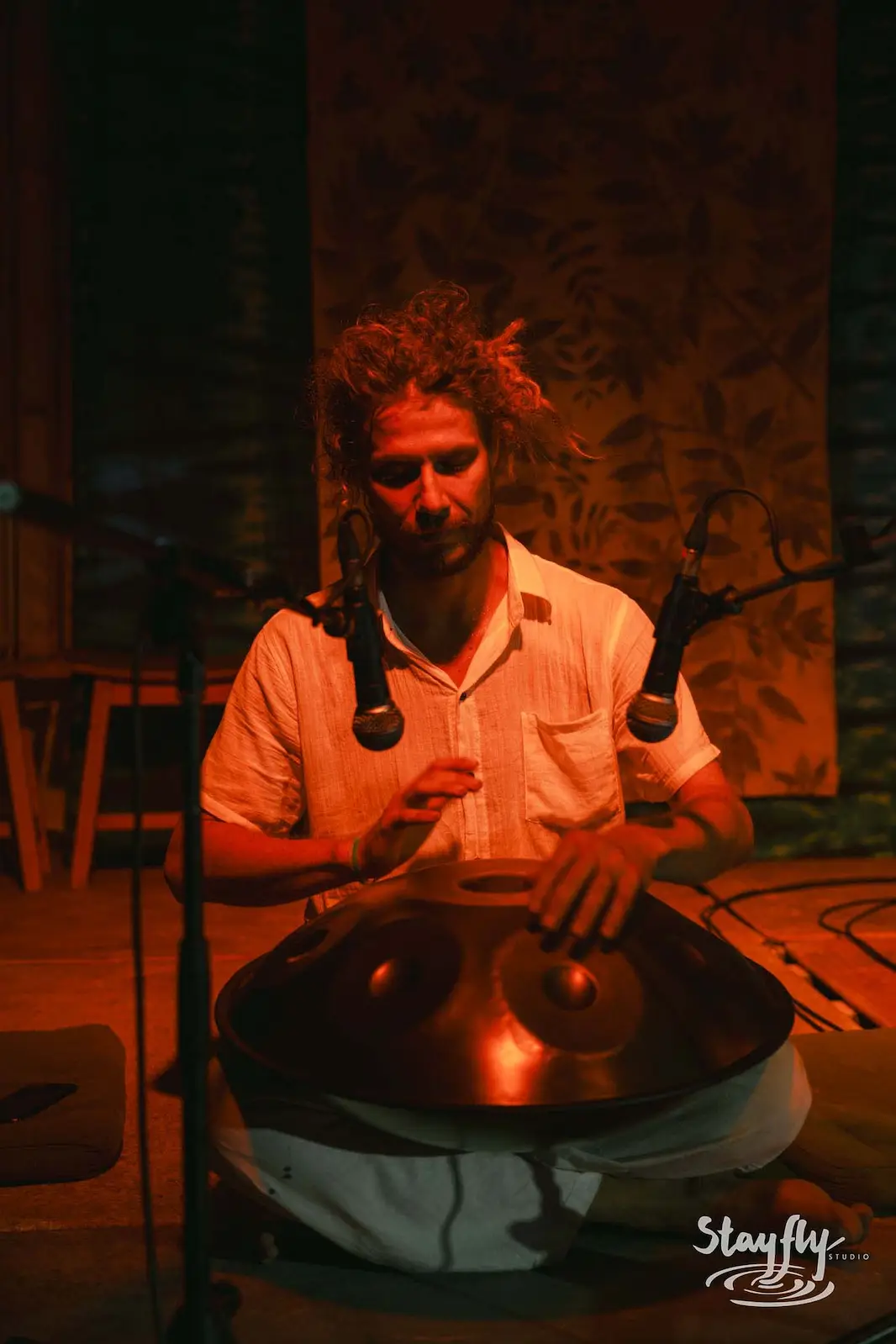 Man playing handpan on small lit stage.