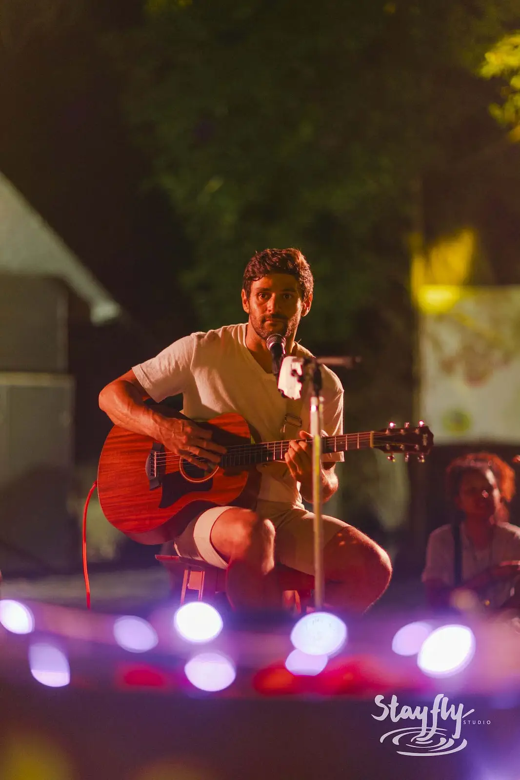 Man playing acoustic guitar on stage at night.