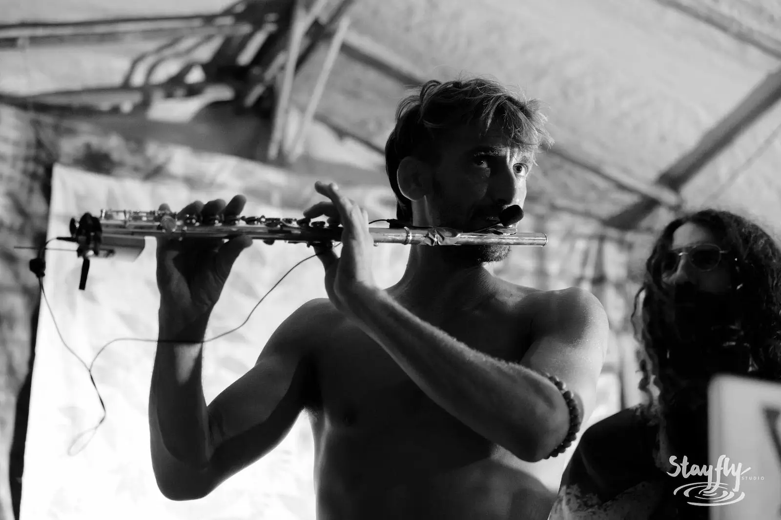 Shirtless flutist playing, black and white indoor shot.