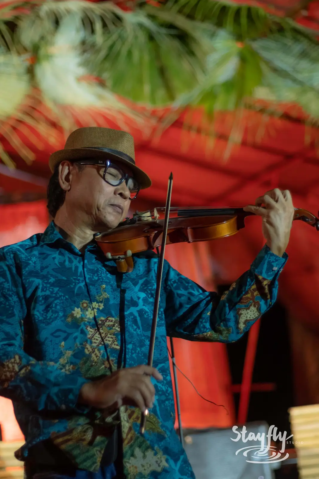 Violinist in hat performing under red canopy.